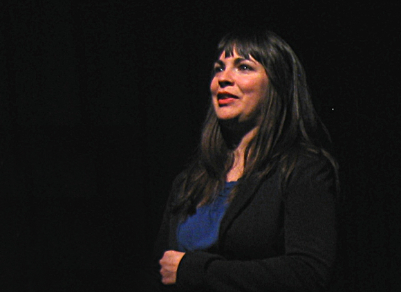 A woman stands on stage speaking.